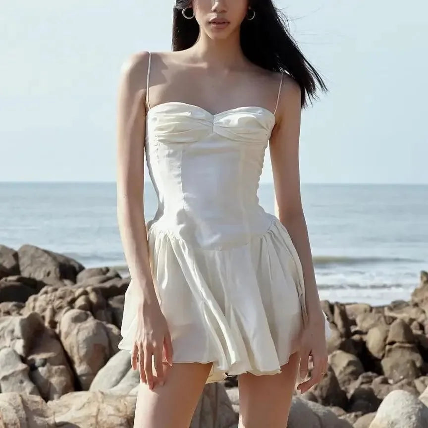 Cream mini dress with a sweetheart neckline, adjustable straps, and a flared skirt, styled for a beach outing.