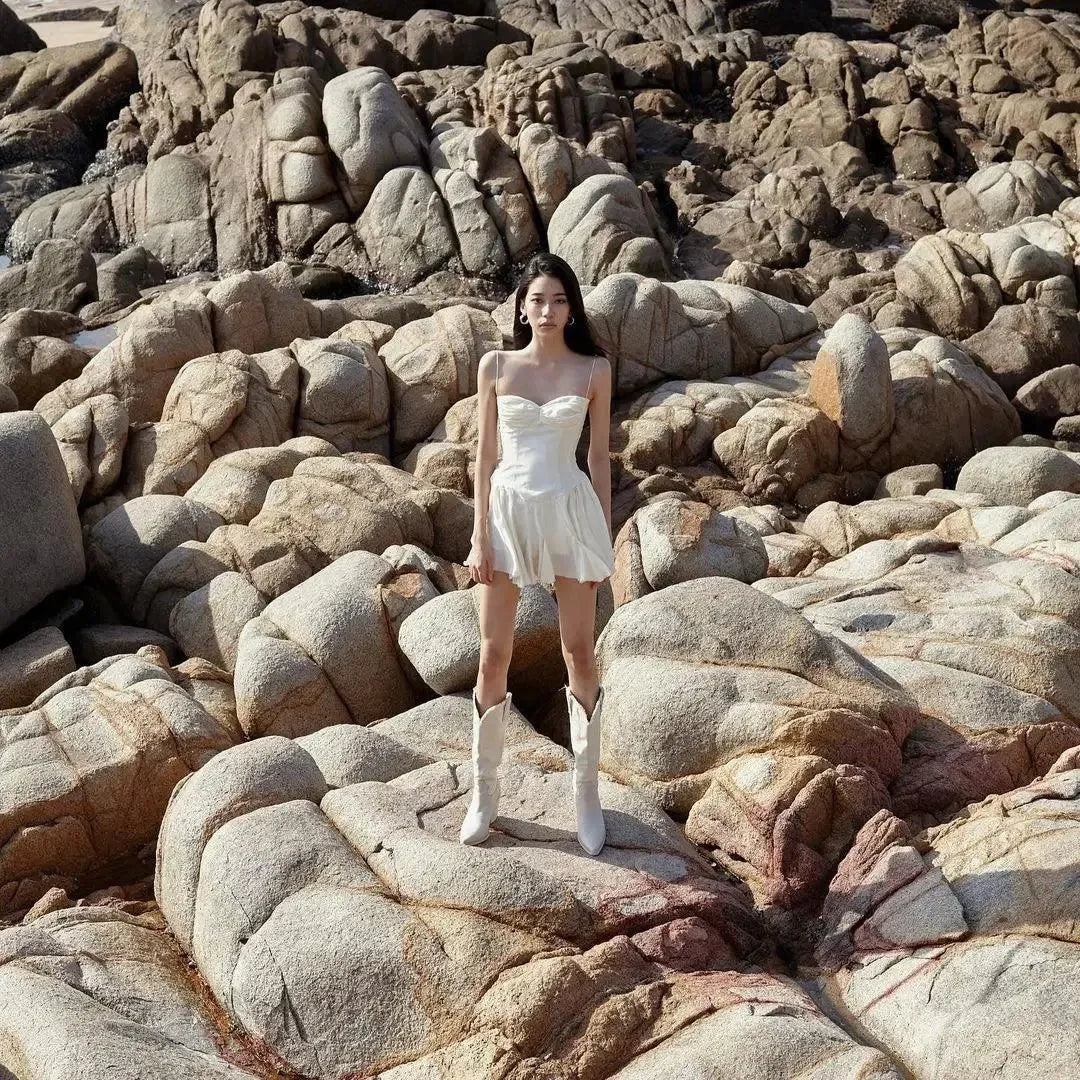 Strapless white mini dress with a flared skirt, styled with knee-high white boots, perfect for a chic summer look.