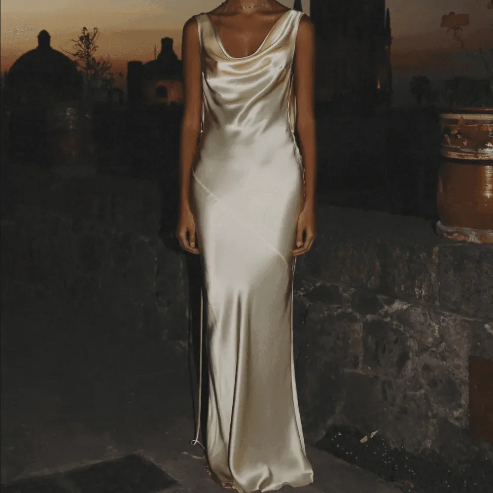 Silky cream maxi dress with a plunging back and cowl neckline, elegantly worn for a chic evening look.