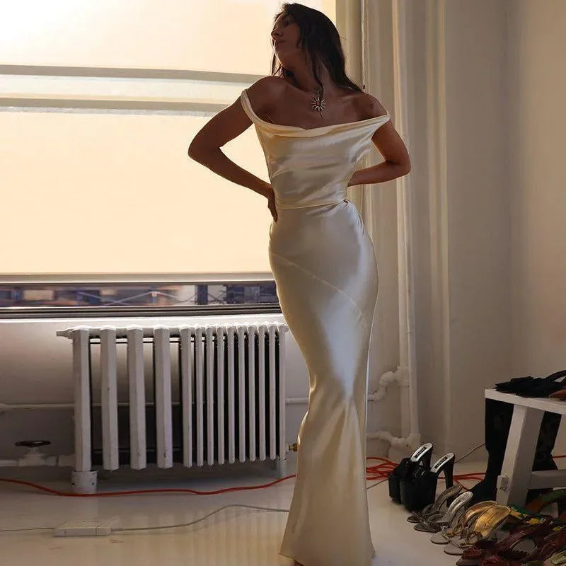 Elegant cream cowl maxi dress with a plunging back, styled off the shoulders for a sophisticated evening look.