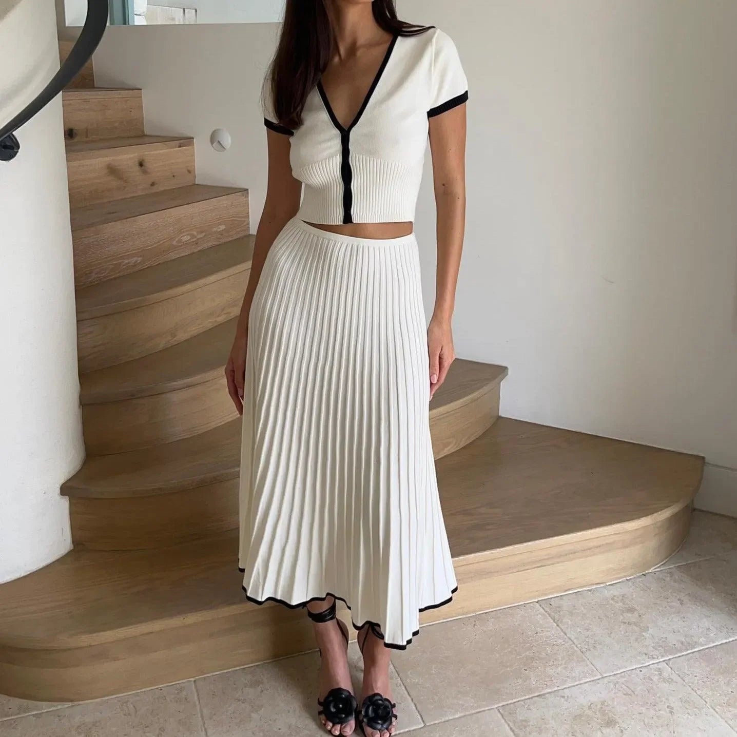 White pleated two-piece set featuring black contrast trim, styled with a fitted cropped top and flowing midi skirt.
