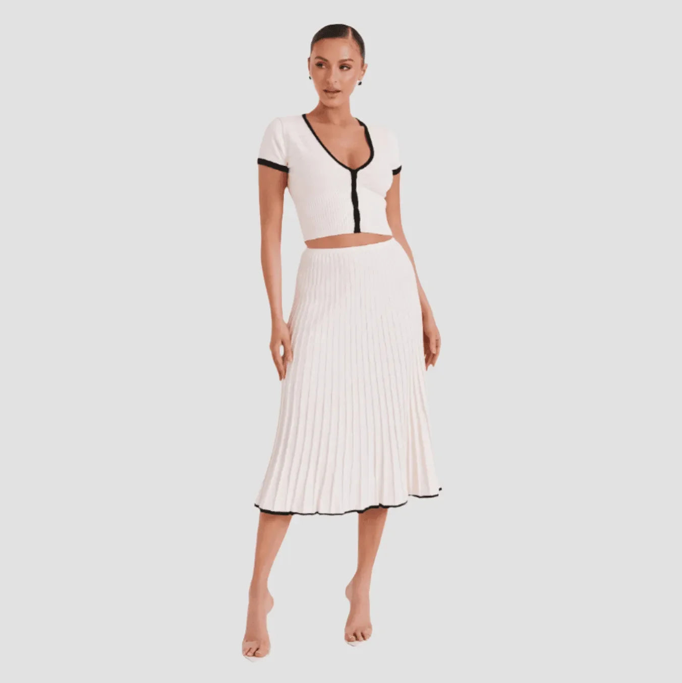 White two-piece set featuring a cropped top with black trim and pleated midi skirt, styled for a chic evening look.