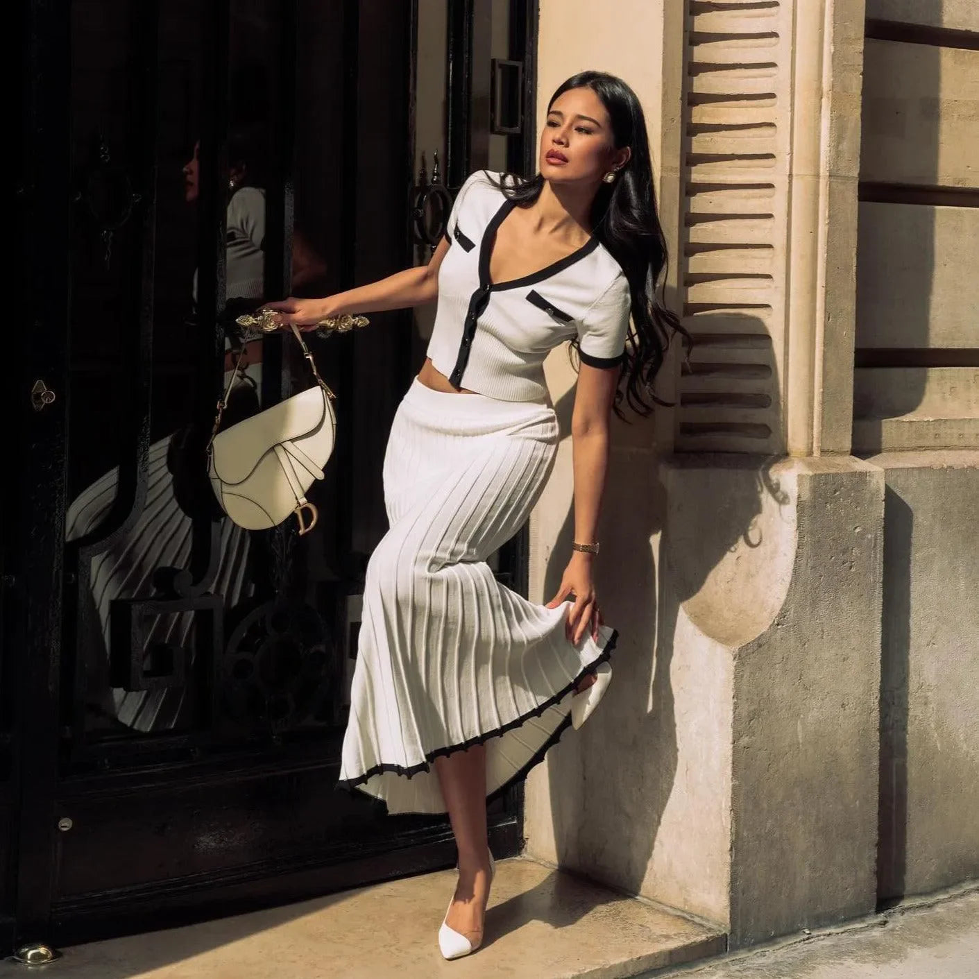 Black and white contrast knit two-piece set featuring a cropped top and pleated midi skirt, styled with a chic handbag.