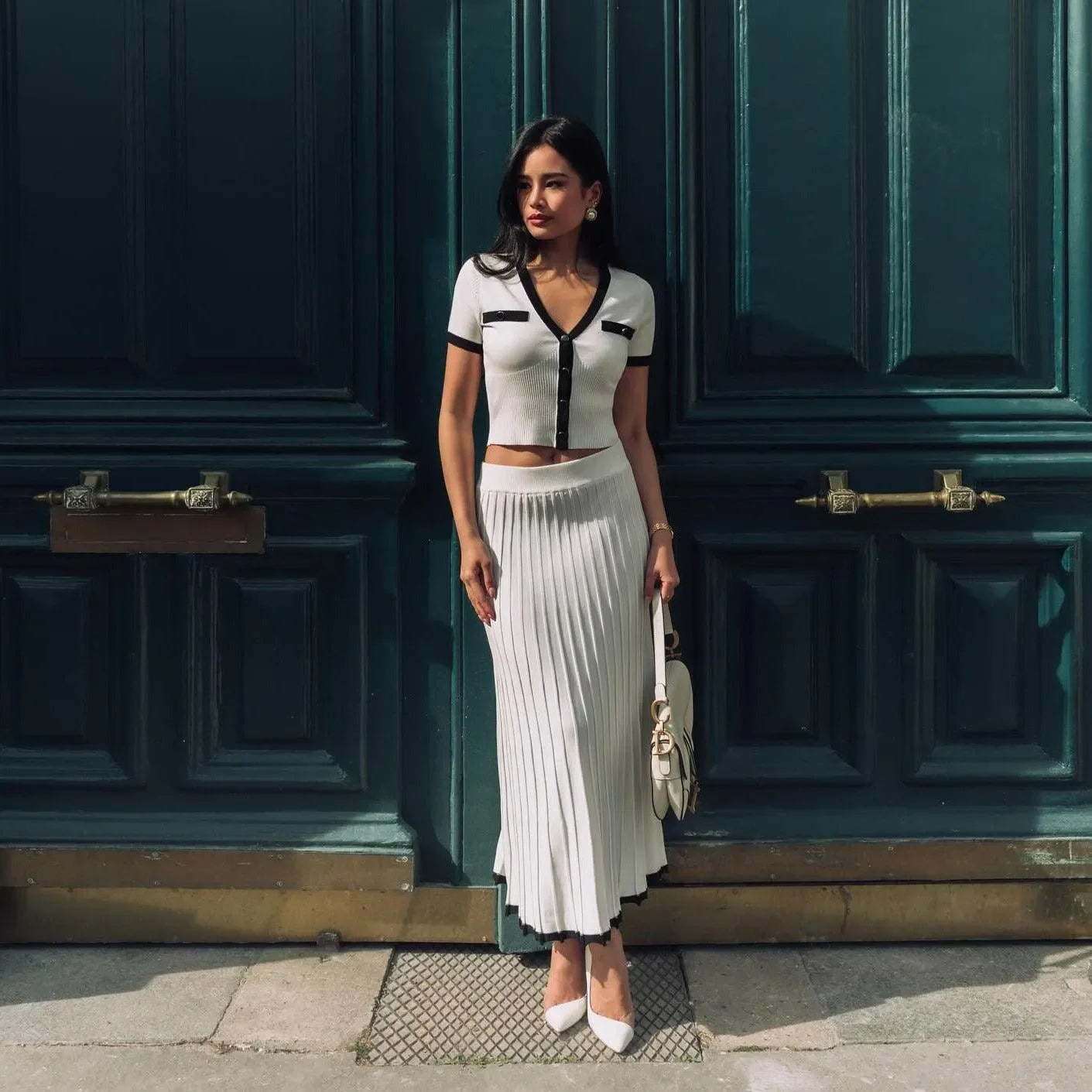 Chic two-piece set featuring a cropped white top with black accents and a pleated midi skirt, styled with heels.