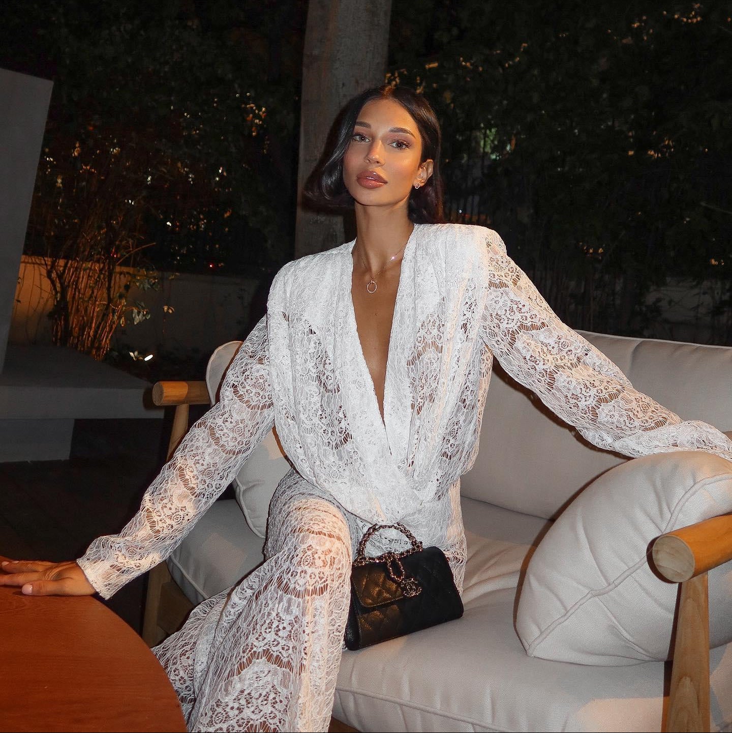 White lace two-piece set featuring a deep V-neck and long sleeves, styled effortlessly with a chic handbag.