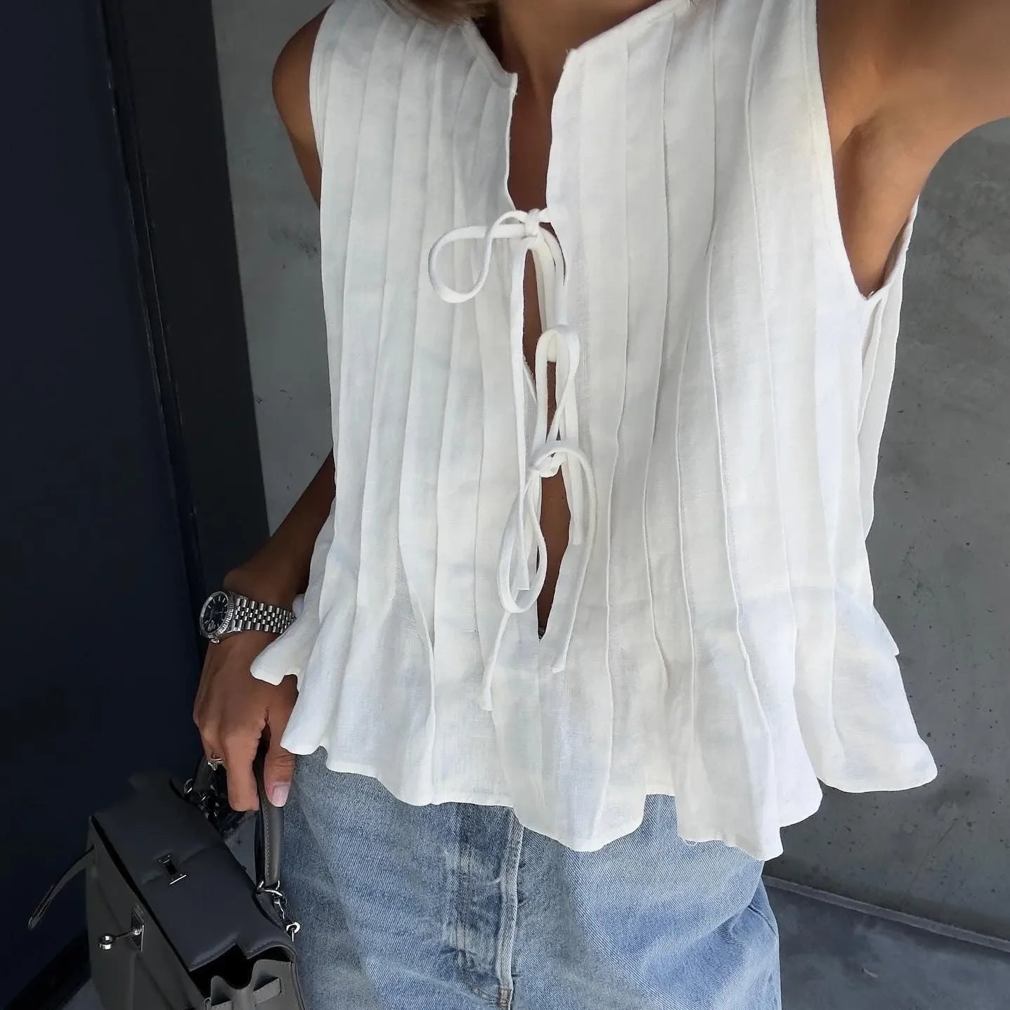 White pleated cotton top with a keyhole tie closure, styled with a flared hem, paired with a denim skirt.