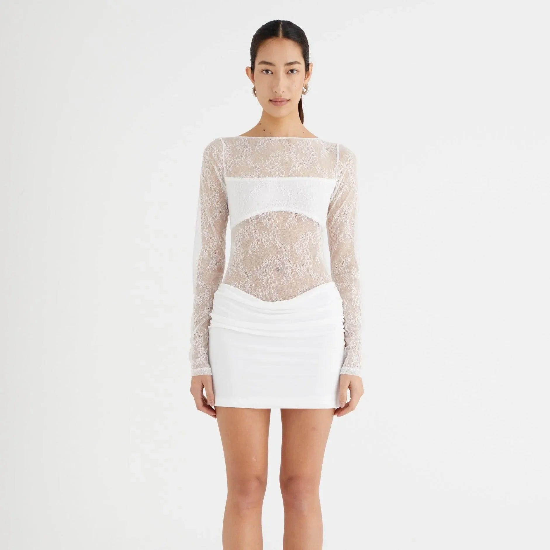 White lace mini dress with long sleeves and ruched detailing, styled with a fitted silhouette for a playful look.