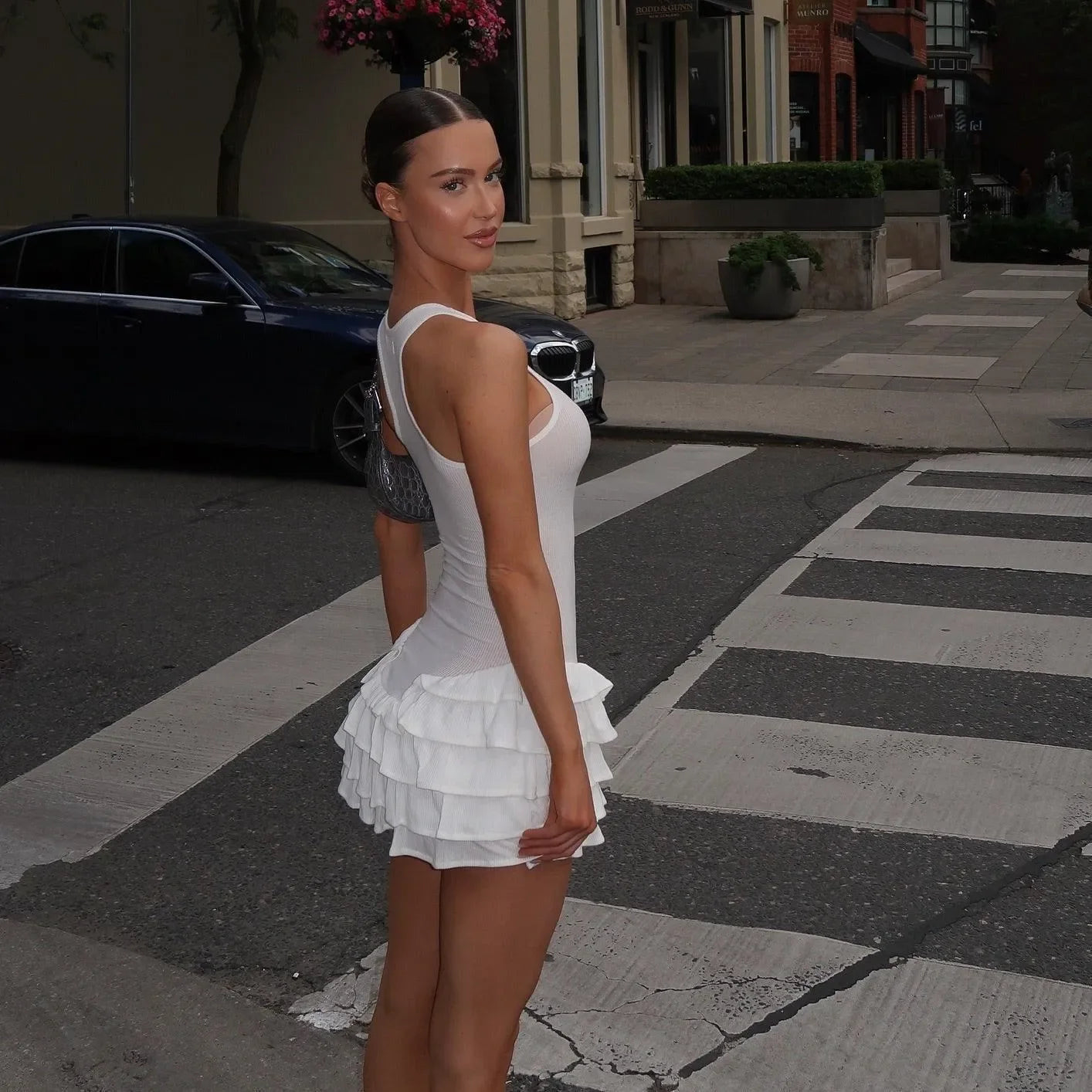 White mini dress featuring frill hem and a fitted silhouette, styled with sleek hair for a chic, modern look.