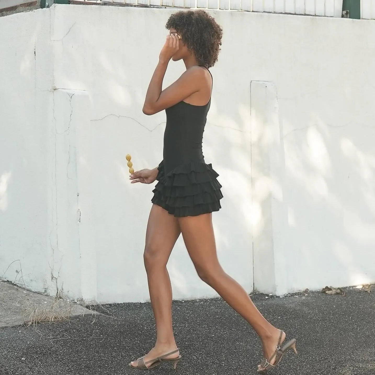 Black mini dress with frills, sleeveless design, styled casually with sandals, perfect for warm weather outings.