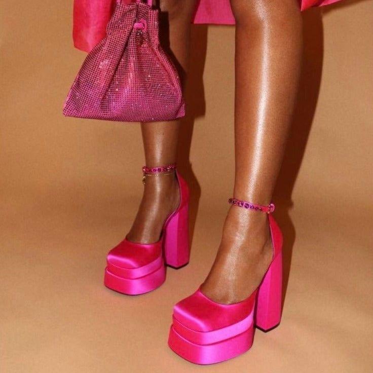 Person wearing bright pink platform shoes and matching handbag on a beige background