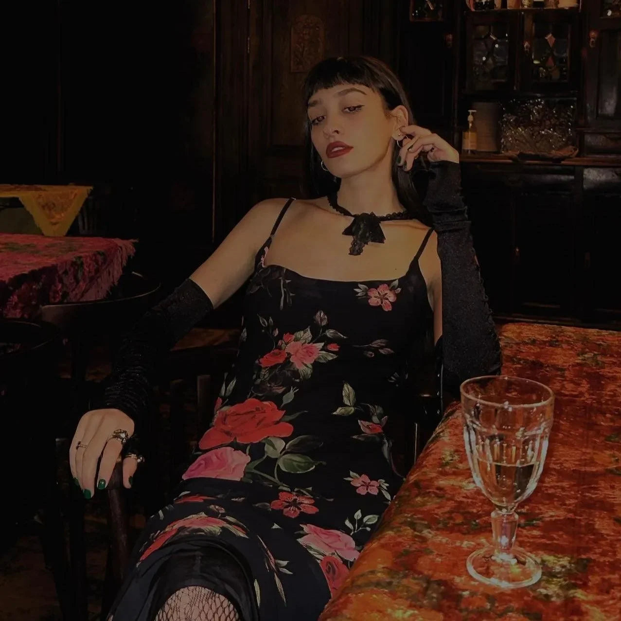 Black floral maxi dress with spaghetti straps, styled with lace gloves and a choker for an elegant evening look.