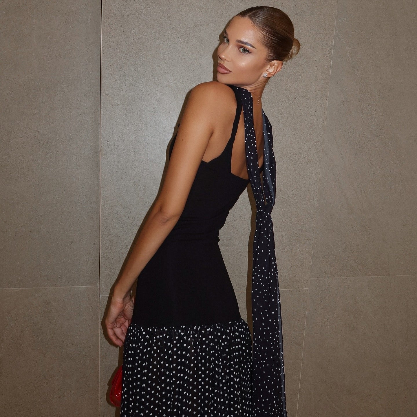 Black maxi dress with polka dot skirt and scarf detail, styled with a pulled-back hairstyle for an elegant look.