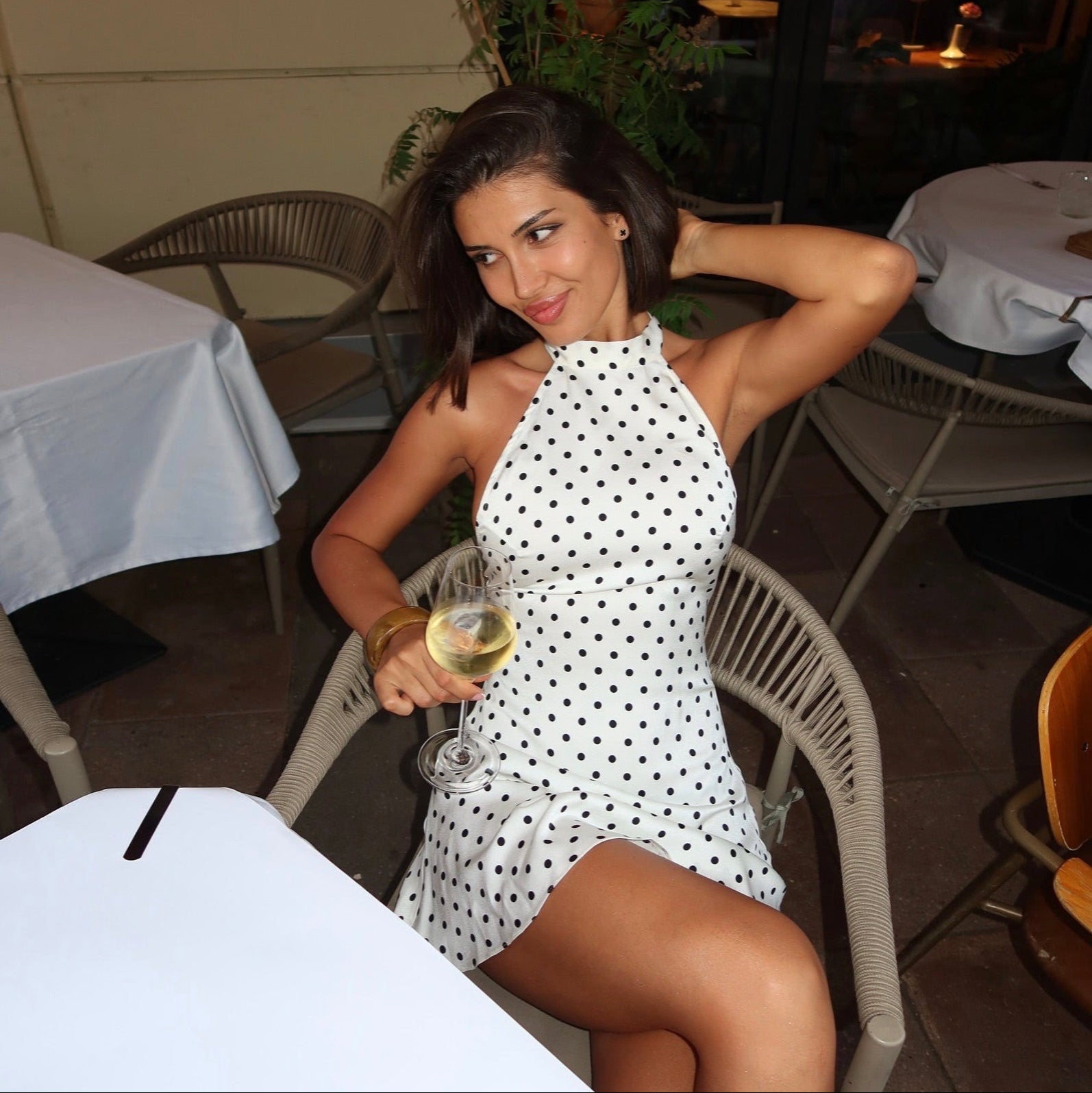 White halter mini dress with black polka dots, fitted bodice, flared skirt, styled for a casual outdoor gathering.