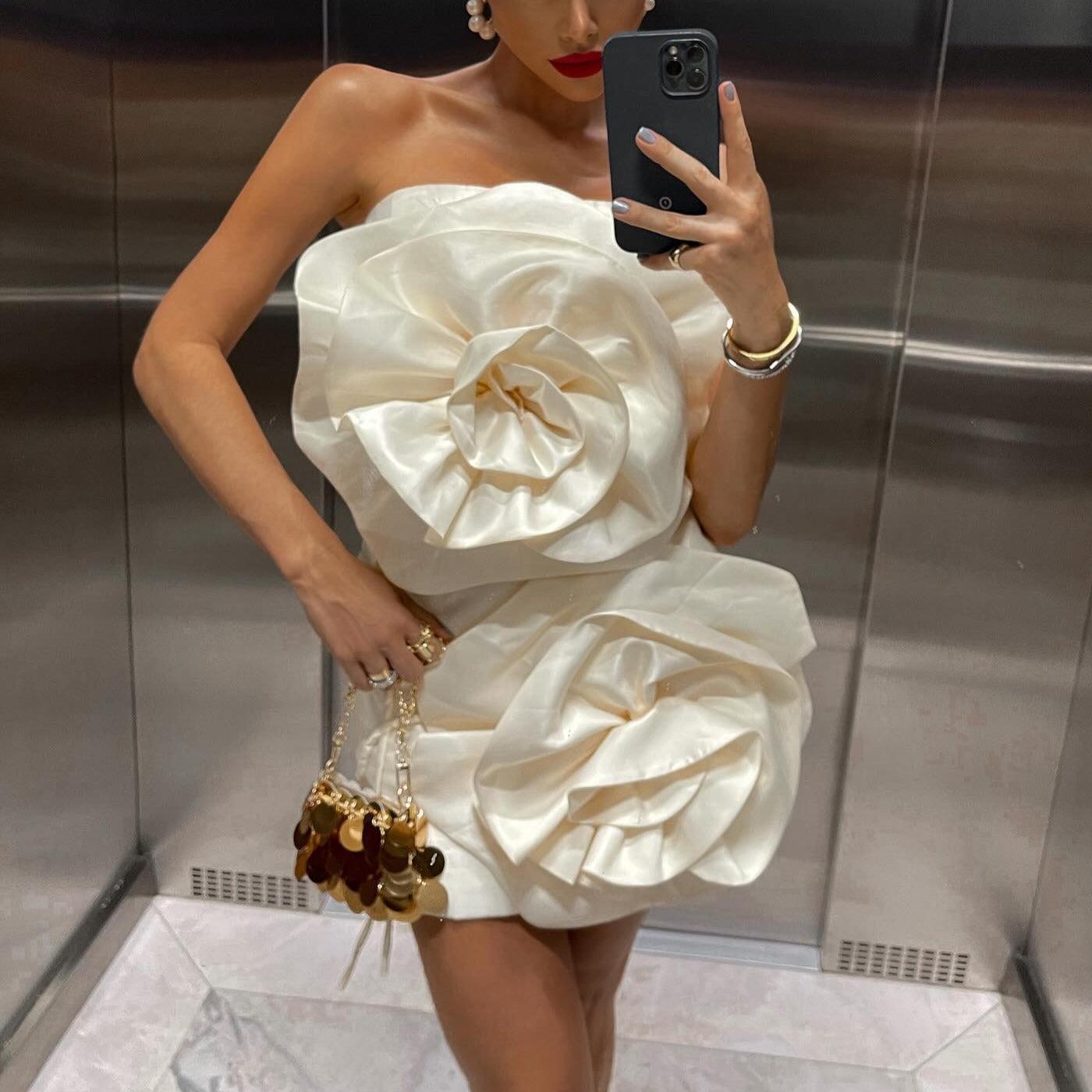 Strapless ivory mini dress with voluminous flower accents, styled with statement earrings and a clutch.