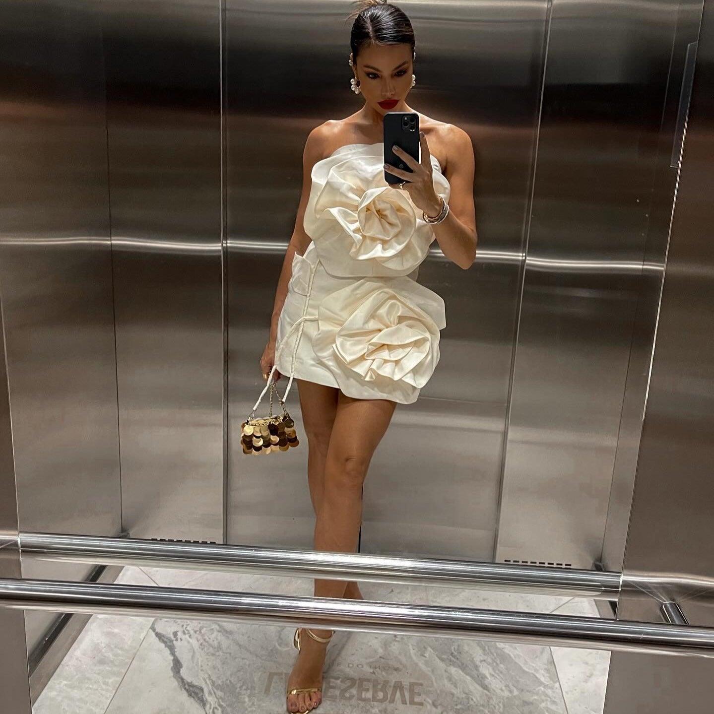 Strapless ivory mini dress featuring large flower appliqués, styled with a small handbag and high heels for an elegant look.