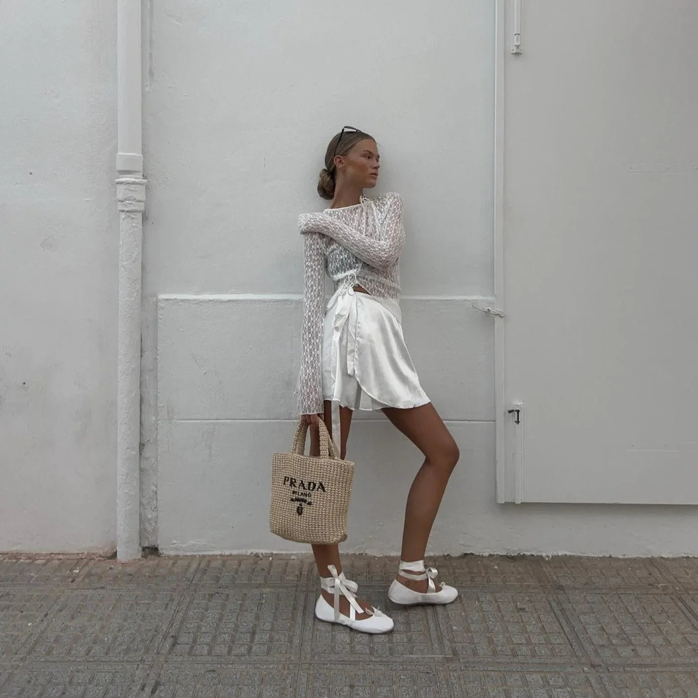 White floral lace trim top styled with a satin mini skirt and strappy sandals, paired with a woven tote bag.