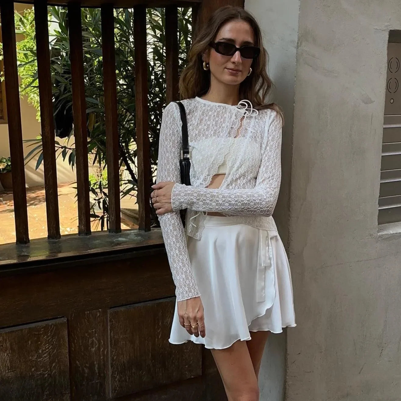 White floral lace trim top with long sleeves, styled with a high-waisted skirt and sunglasses for a chic look.