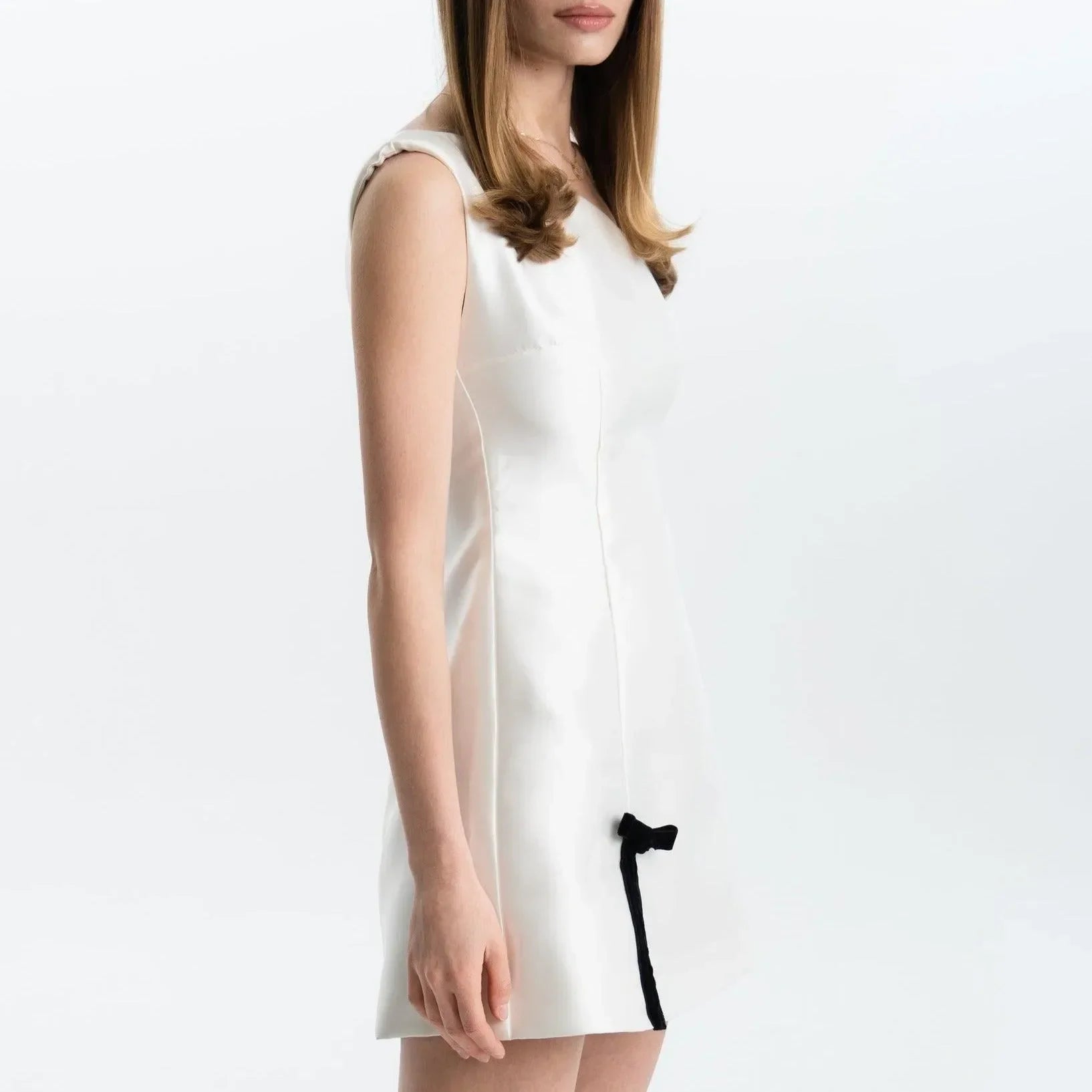 White satin mini dress featuring a slim fit and a black bow detail, styled with a sleek silhouette for a chic look.