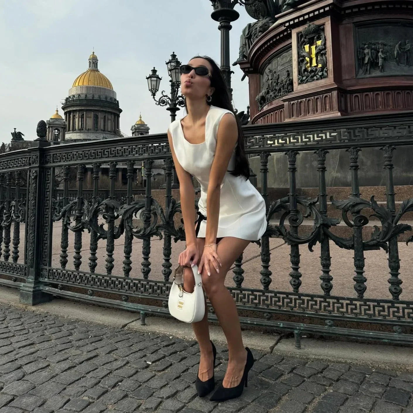 White satin mini dress with a fitted silhouette, styled with black heels and a chic handbag, perfect for summer outings.