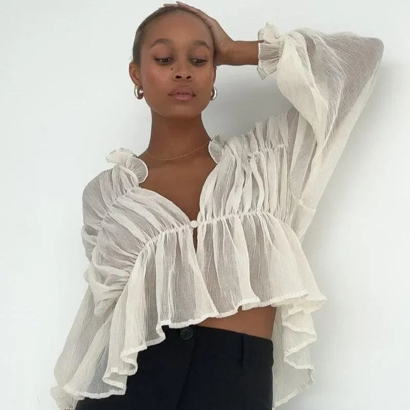 Ivory long sleeve semi-sheer top with ruffled hem and puff sleeves, styled casually with high-waisted trousers.