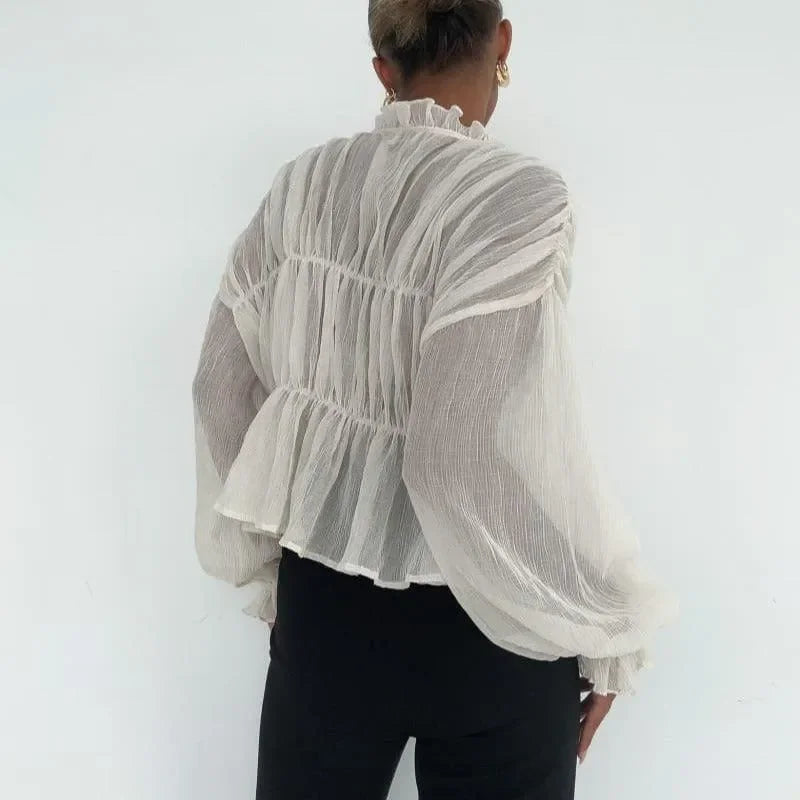 Ivory long sleeve top with semi-sheer fabric, ruffled neckline, and peplum hem, styled with fitted black pants.