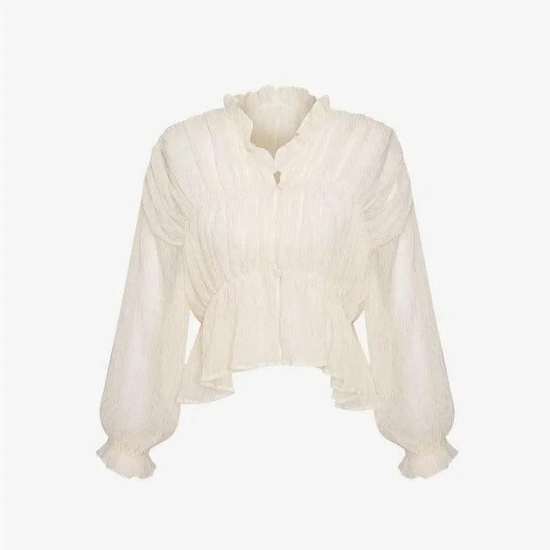 Ivory long sleeve semi-sheer top with ruffled neckline and textured fabric, styled with high-waisted jeans for a chic look.
