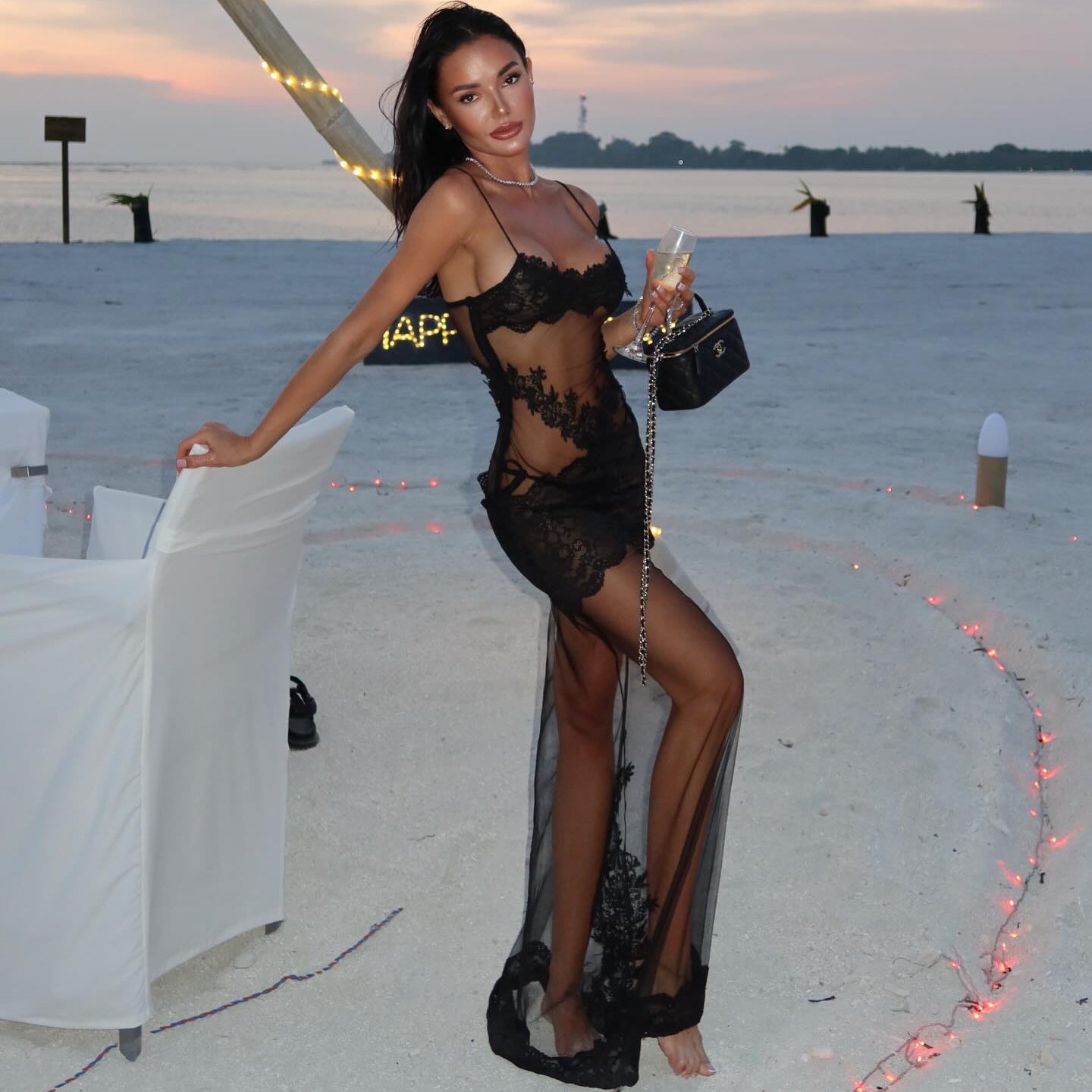 Woman in a sheer black dress standing on a beach with a sunset background