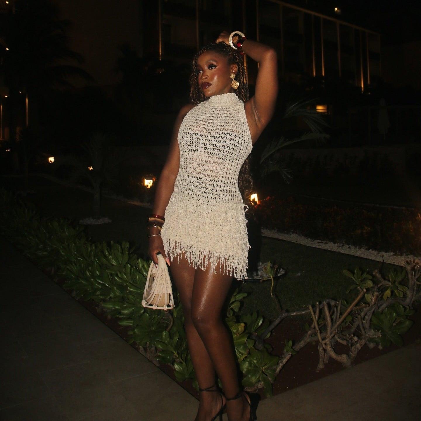 Beige knitted mini dress with fringe hemline, styled with strappy heels and accessories for a chic evening look.