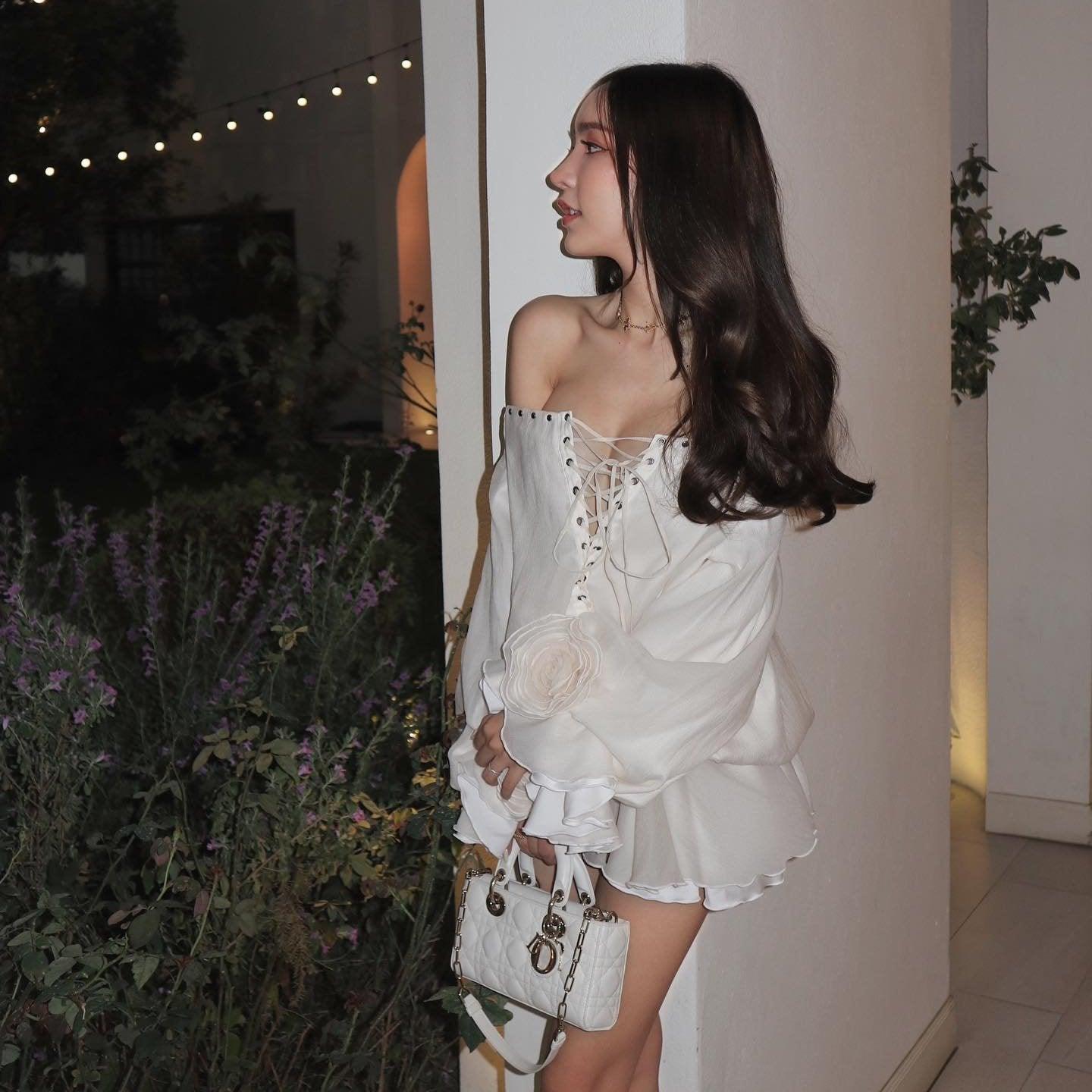 White off-shoulder mini dress with lace-up front and ruffled hem, styled with a chic handbag for a night out.