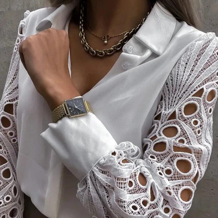Elegant white blouse with lace-paneled sleeves, styled with layered necklaces and a classic watch for a chic look.