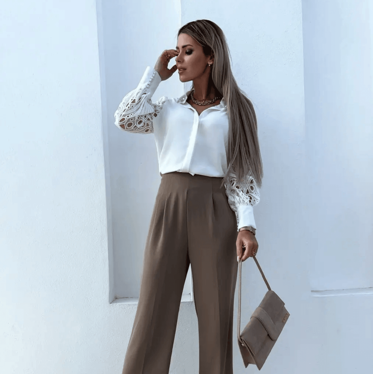 White lace satin blouse with button-down front and detailed sleeves, styled with high-waisted beige trousers and a handbag.