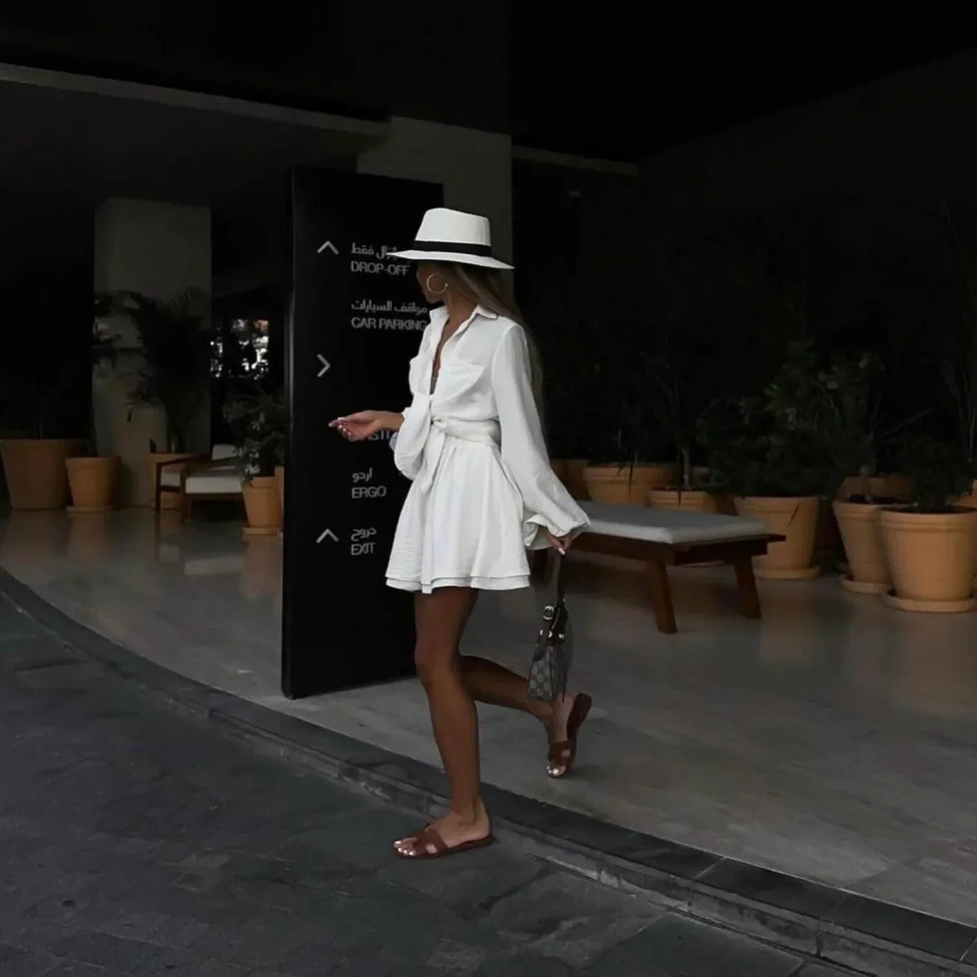 White two-piece set featuring a wrap blouse and mini skirt, styled with a wide-brimmed hat and sandals for a chic look.