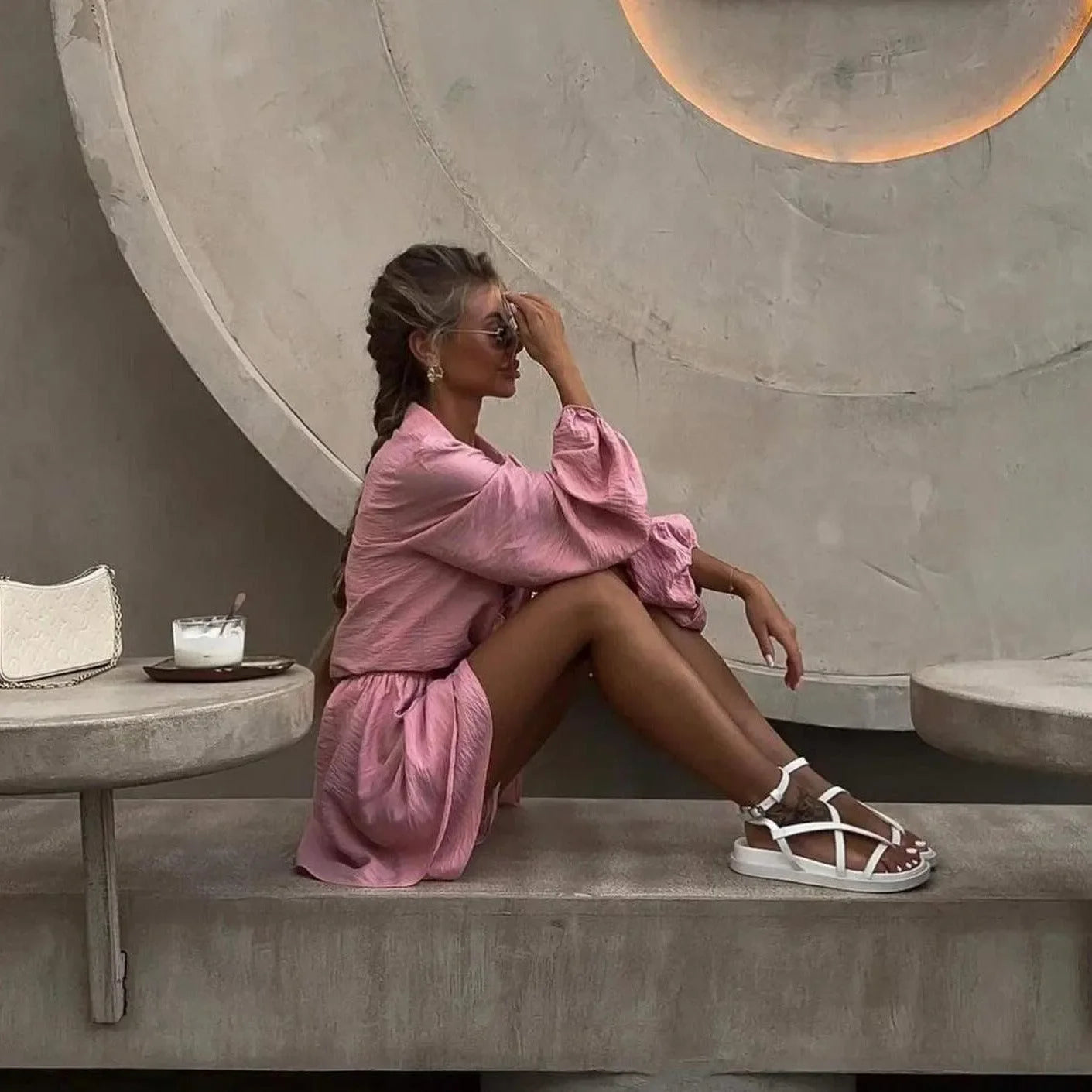 Pink two-piece set featuring a flowy long-sleeve blouse and mini skirt, styled with chic sandals and sunglasses.