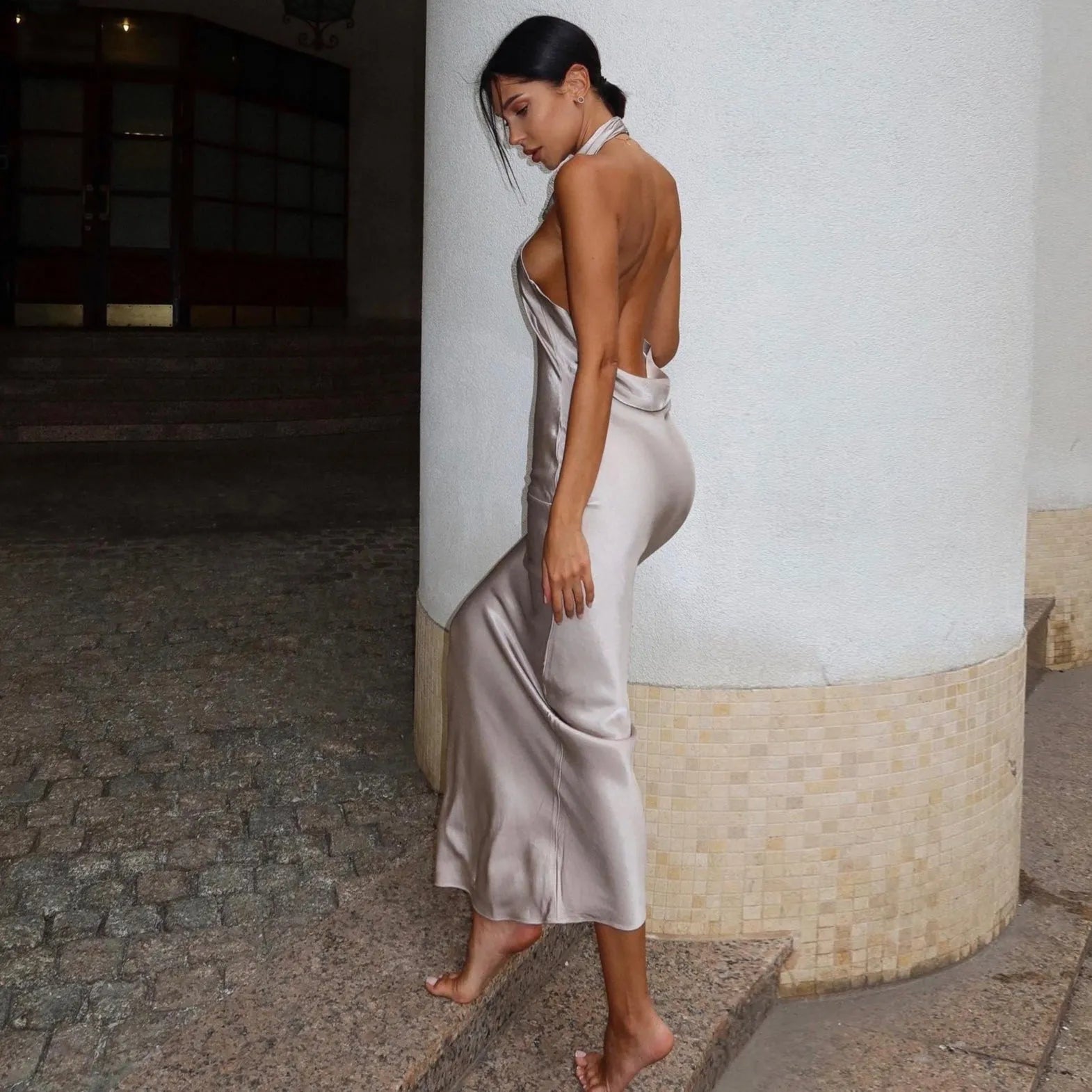 Satin backless maxi dress in soft nude, featuring a halter neckline, flowing silhouette, elegantly styled for a chic look.