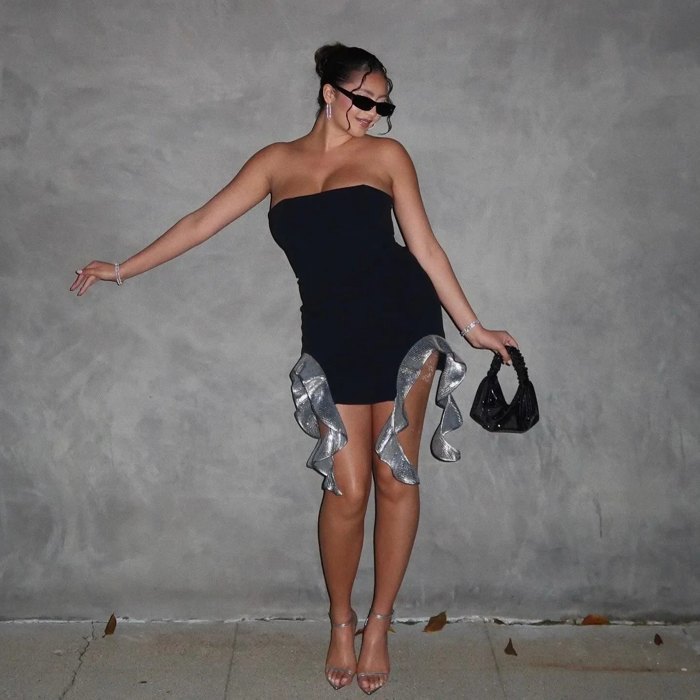 Strapless black mini dress with sequined ruffles, styled with sleek sunglasses and a chic handbag for a night out.