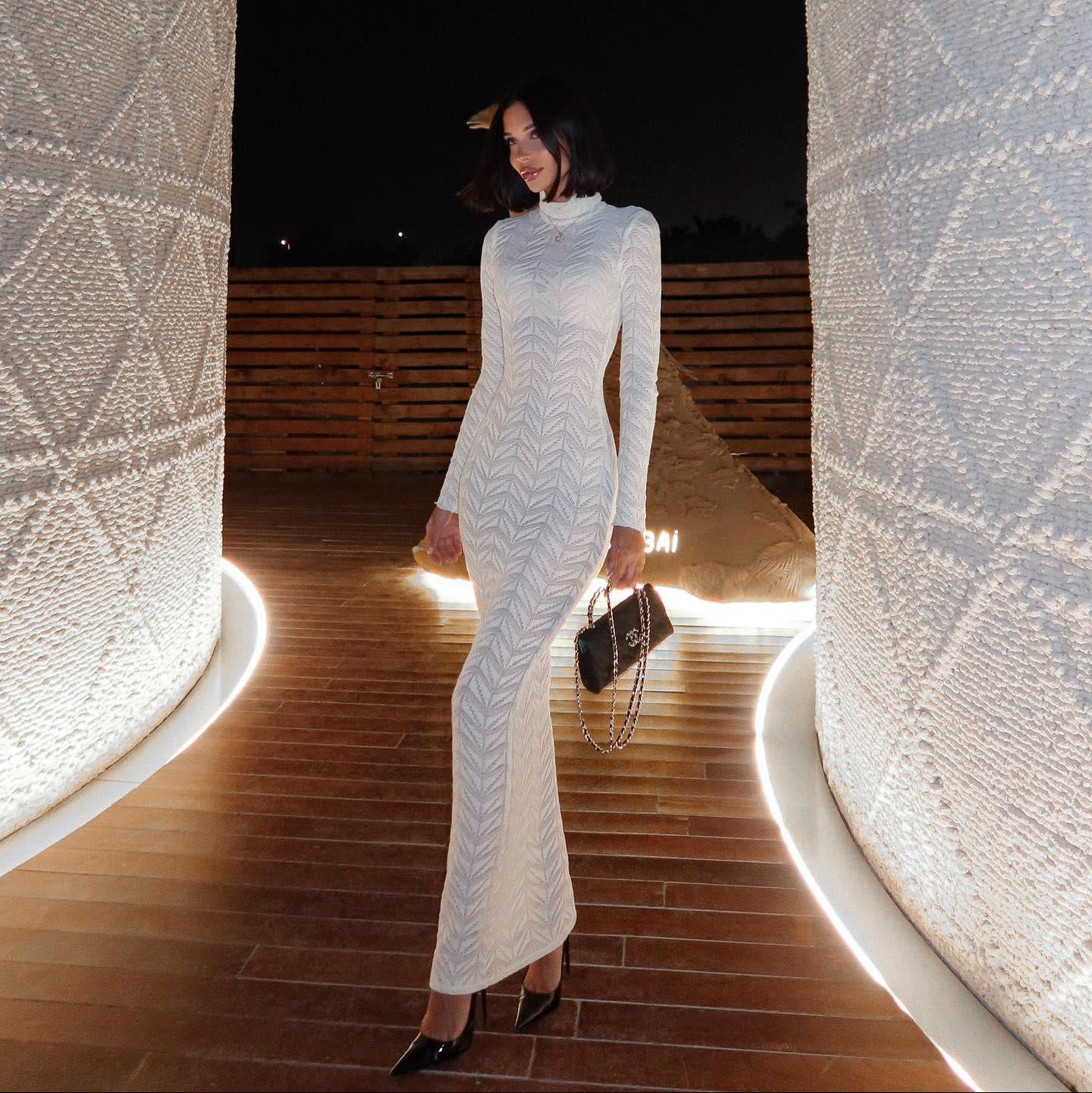 White knitted turtleneck maxi dress with long sleeves, form-fitting silhouette, styled with heels and a clutch.