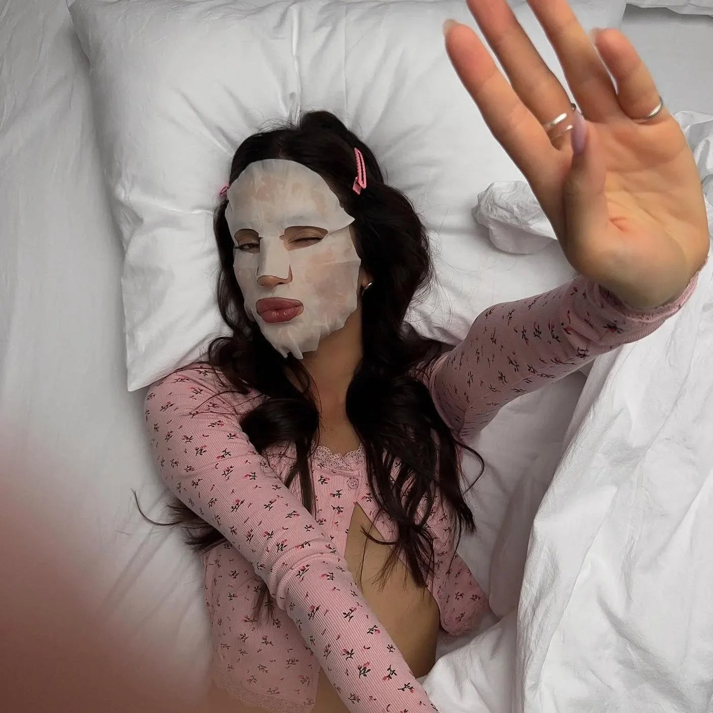 Long-sleeve ribbed pink top with lace trim, paired with matching shorts, styled with a face mask while relaxing.