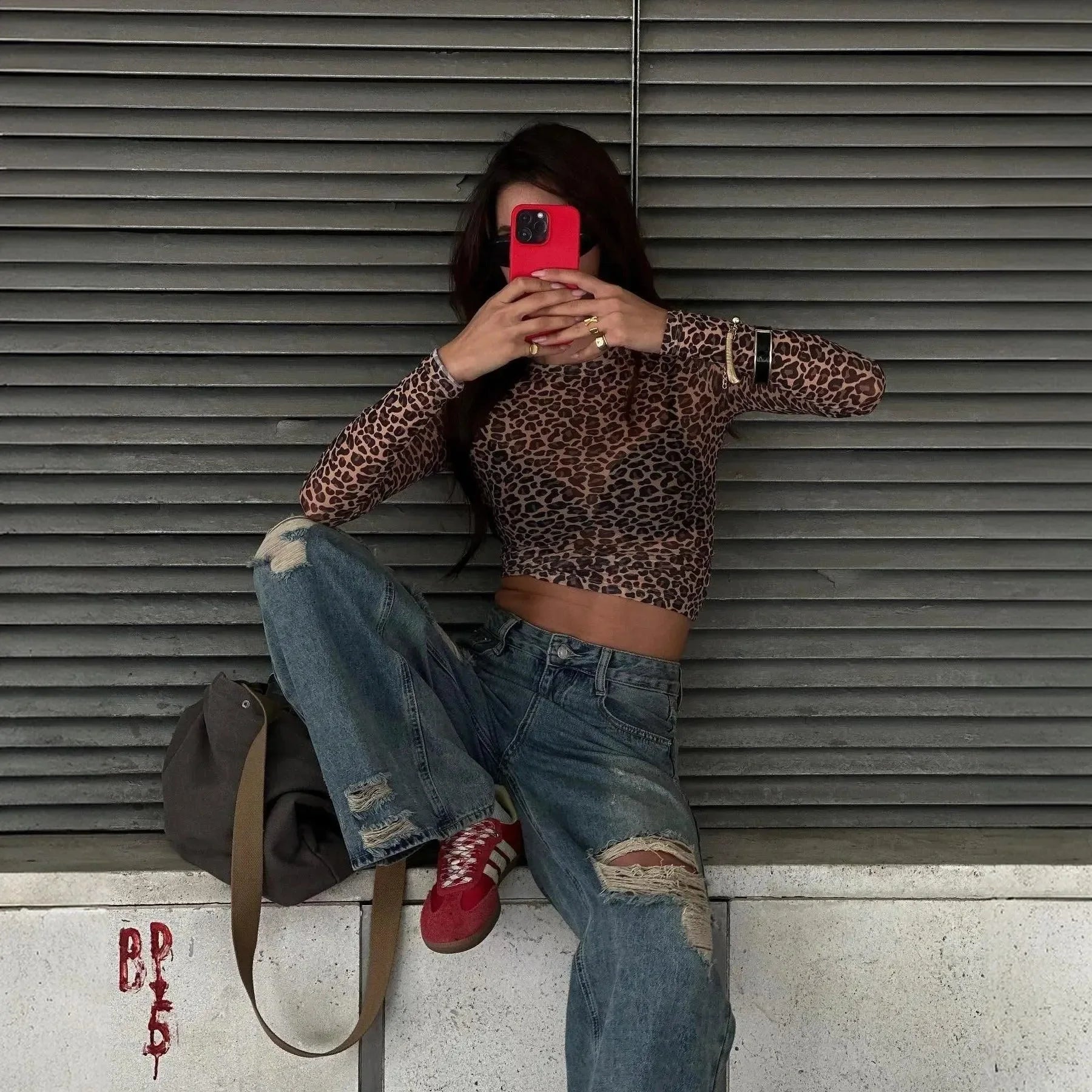 Leopard print long sleeve crop top paired with loose, distressed jeans and red sneakers for a trendy street style look.