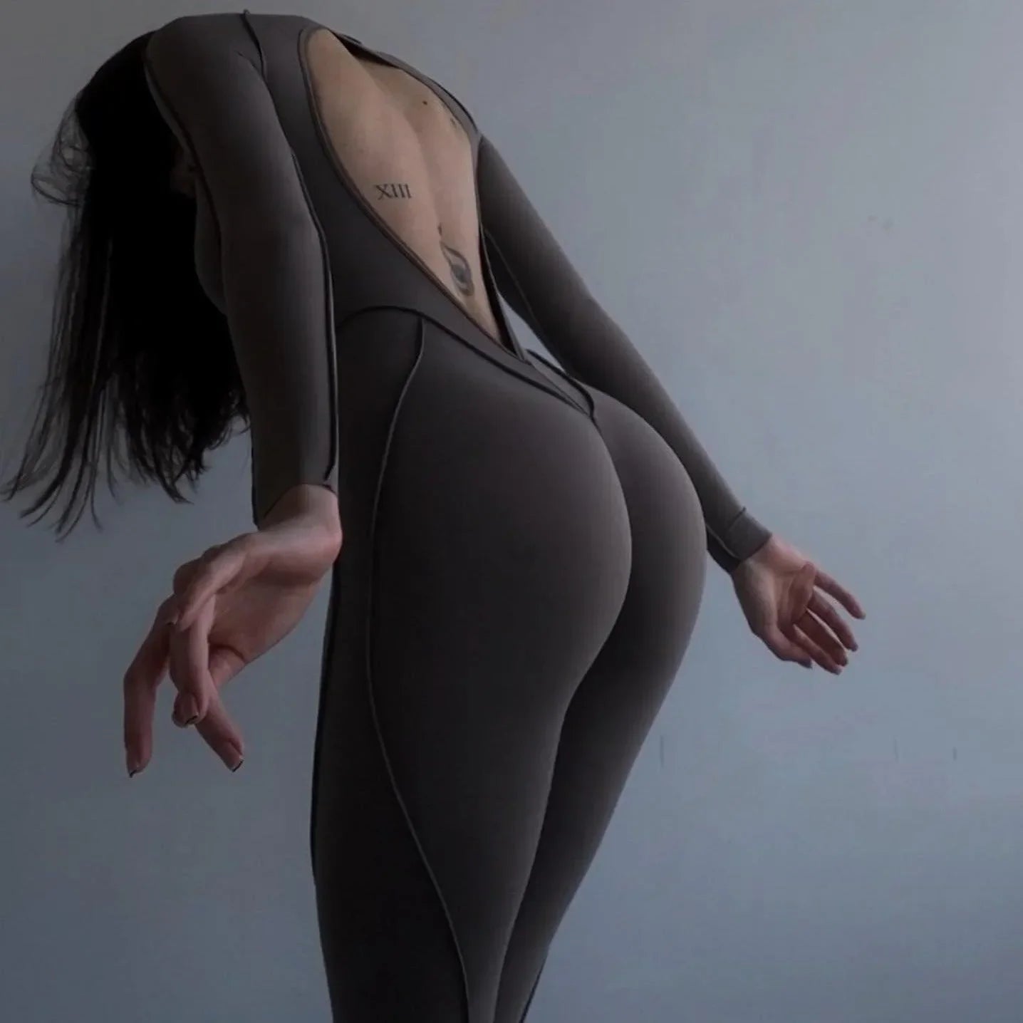 Open back jumpsuit in taupe, features long sleeves and a fitted silhouette, ideal for a chic, edgy look.