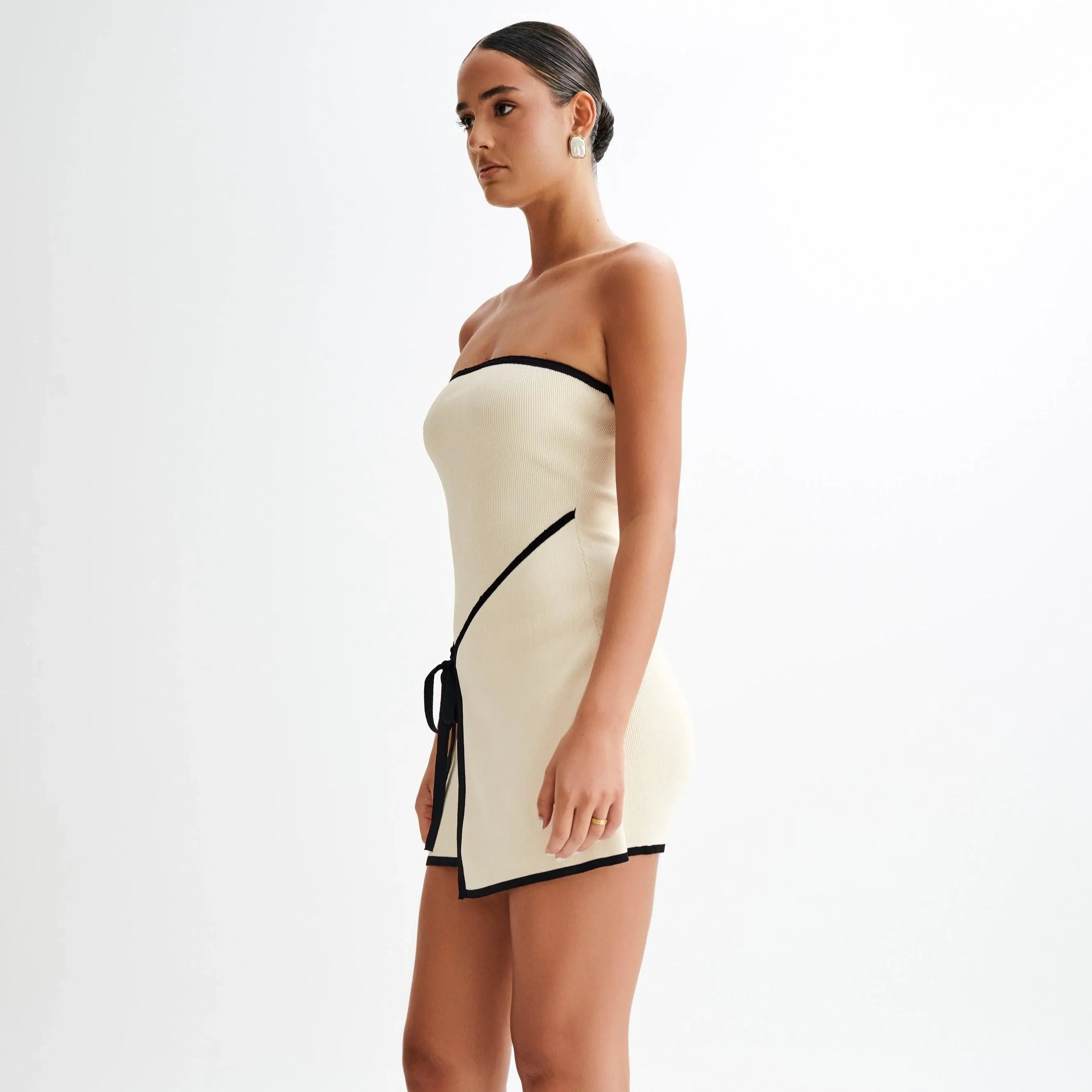 Cream strapless knit mini dress with black trim and a tie detail, styled for a chic and modern look.