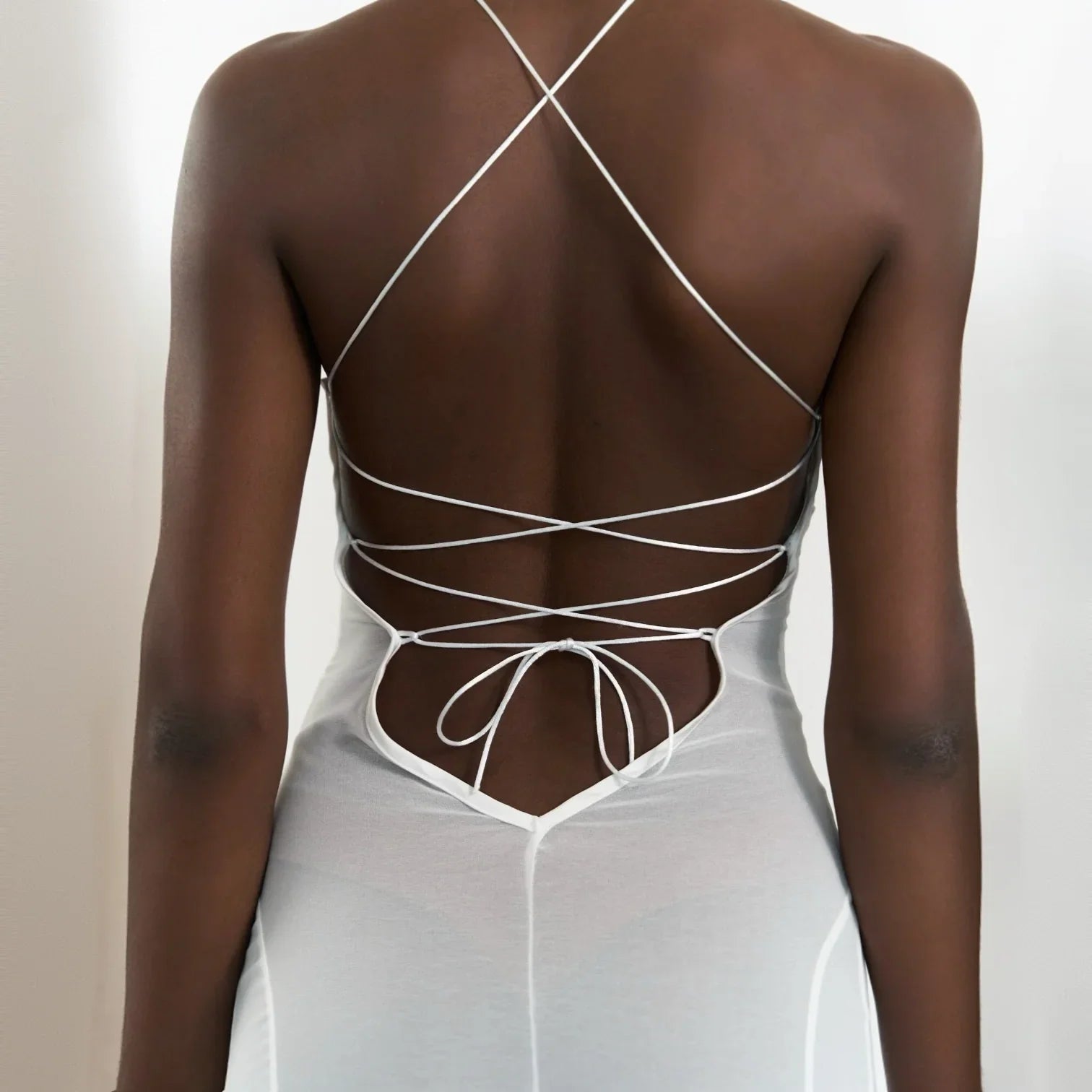 White maxi dress featuring a mesh cutout back and lace-up detail, styled with a crisscross strap design.