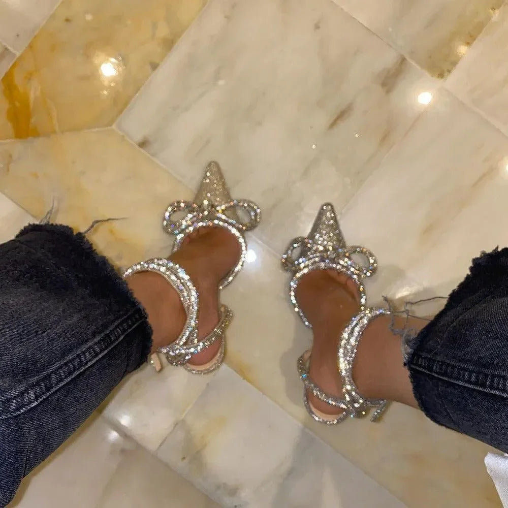 Silver glitter wrap-around bow heels with pointed toes, styled elegantly with cropped denim for a chic look.