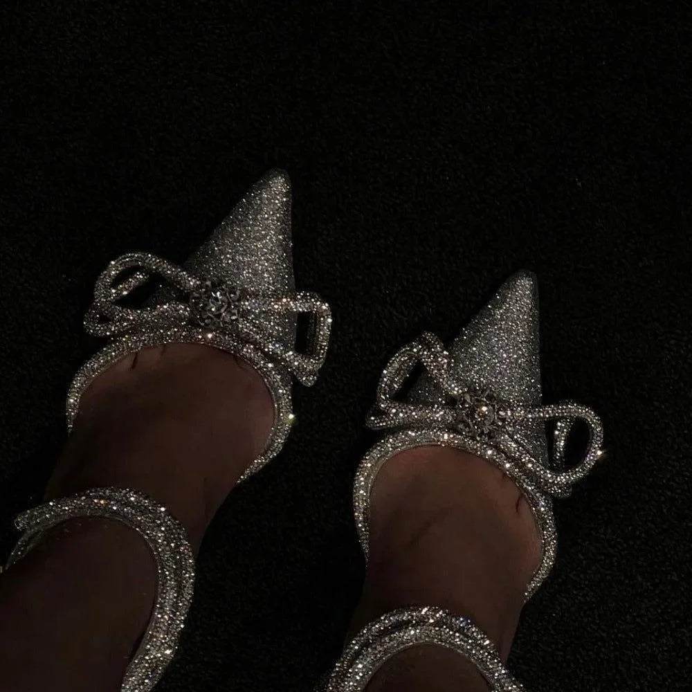 Silver glitter wrap-around bow heels with pointed toes, styled for an elegant, chic look. Perfect for evening wear.