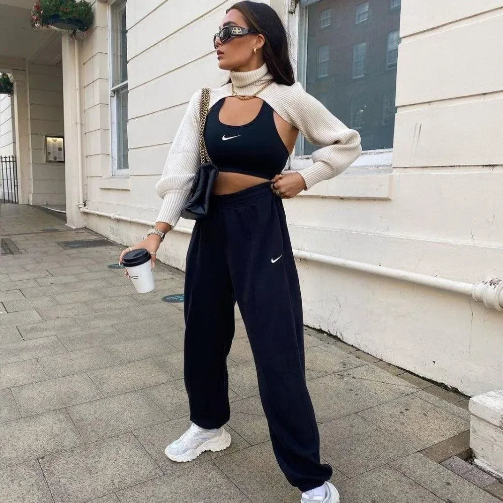 Cream knitted turtleneck crop sweater layered over a black sports bra, paired with black joggers and white sneakers.