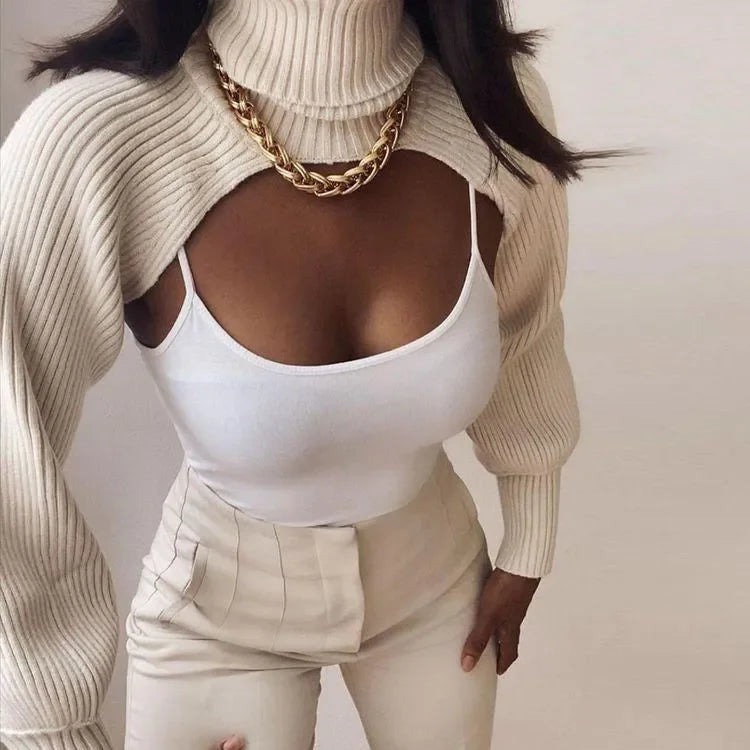 Beige knitted turtleneck crop top with ribbed texture, styled over a white tank and paired with high-waisted trousers.