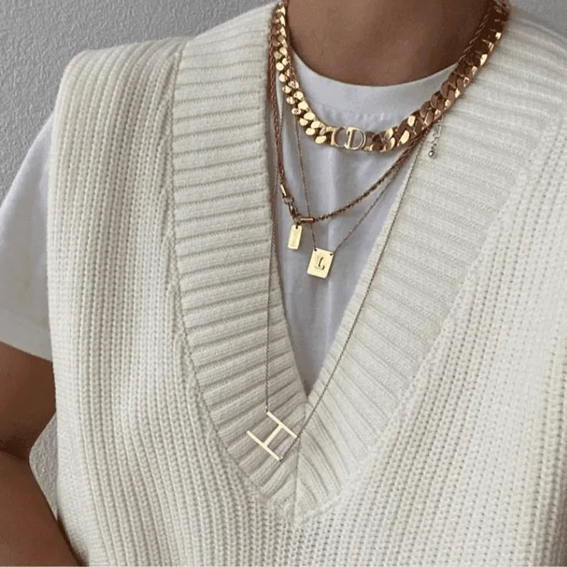 Cream knit sleeveless vest over a white tee with layered gold necklaces.