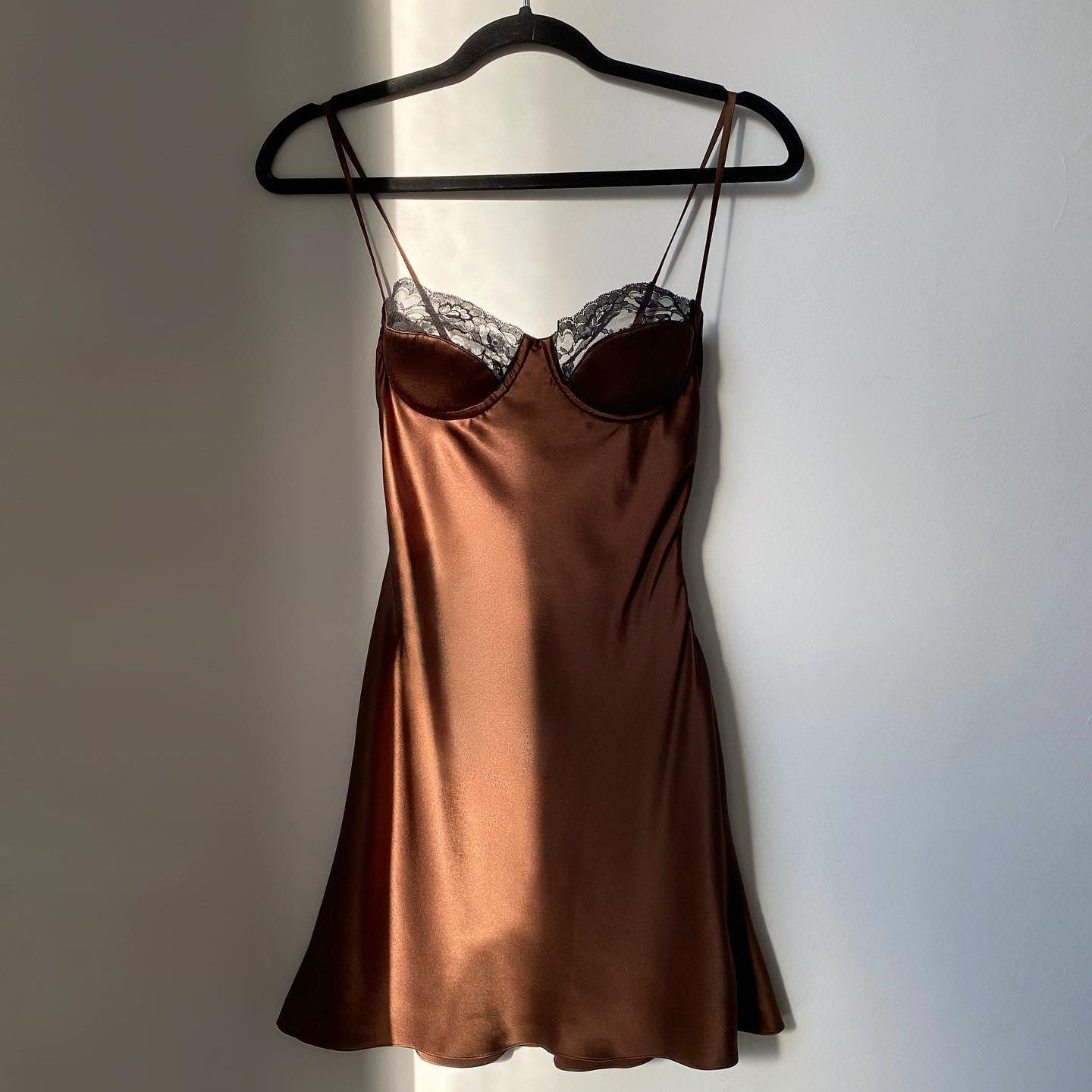 Brown satin slip dress on a hanger against a plain wall