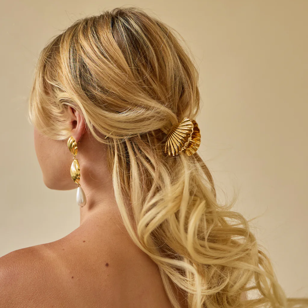 Glossy gold shell metal claw clip securing wavy hair, adding elegance to a chic hairstyle. Perfect for special occasions.
