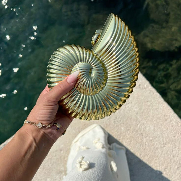 Iridescent conch shell-shaped clutch bag in mint green, elegantly held in hand, perfect for summer outings.