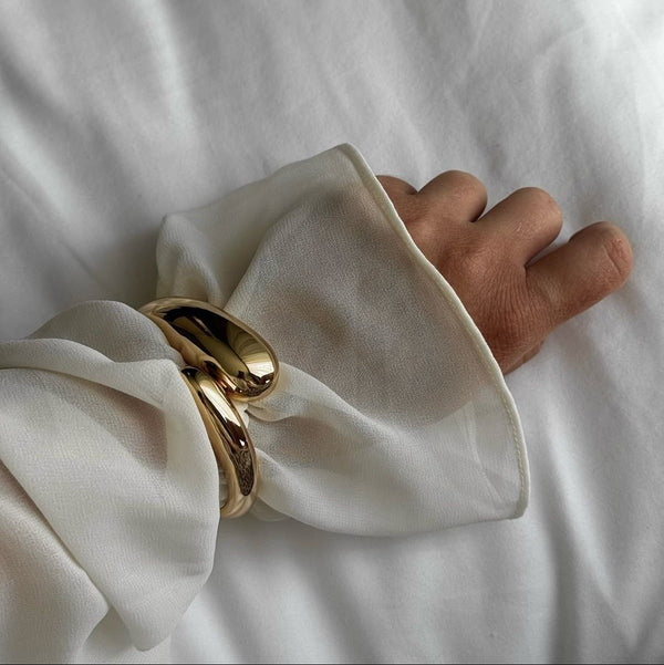 gold cuff bracelet over sheer white sleeve, elegant accessory